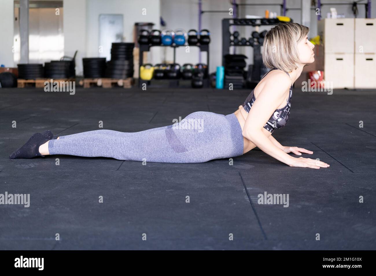 Eine blonde, mittelgroße Erwachsene Frau, die während ihres Vinyasa-Flow-Yoga-Trainings allein eine nach oben gerichtete Hundehaltung mit geschlossenen Augen ausübt, und Leggings und eine Stockfoto