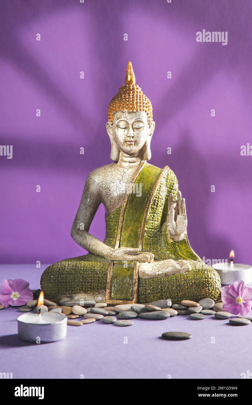 Grüne und goldene buddha-Statue in der Meditation mit Schatten auf hellem lila Hintergrund. Vertikales Format. Stockfoto