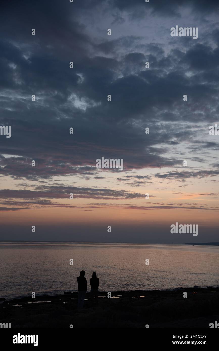 Silhouette eines jungen Paares, das den wunderschönen Sonnenuntergang am Strand genießt. Romantische Moment menschliche Beziehung Stockfoto