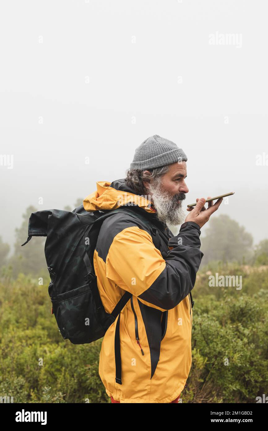 Ein Mann nimmt das Signal auf seinem Handy entgegen und sendet eine Sprachnachricht, Hiker mit Rucksack spricht auf dem Handy während eines Ausflugs Stockfoto