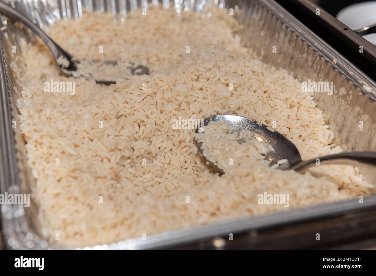 Selbstbedienungsteller mit jasmin-Reis für Gäste, die sich selbst mit den zur Verfügung gestellten Löffeln bedienen können. Stockfoto