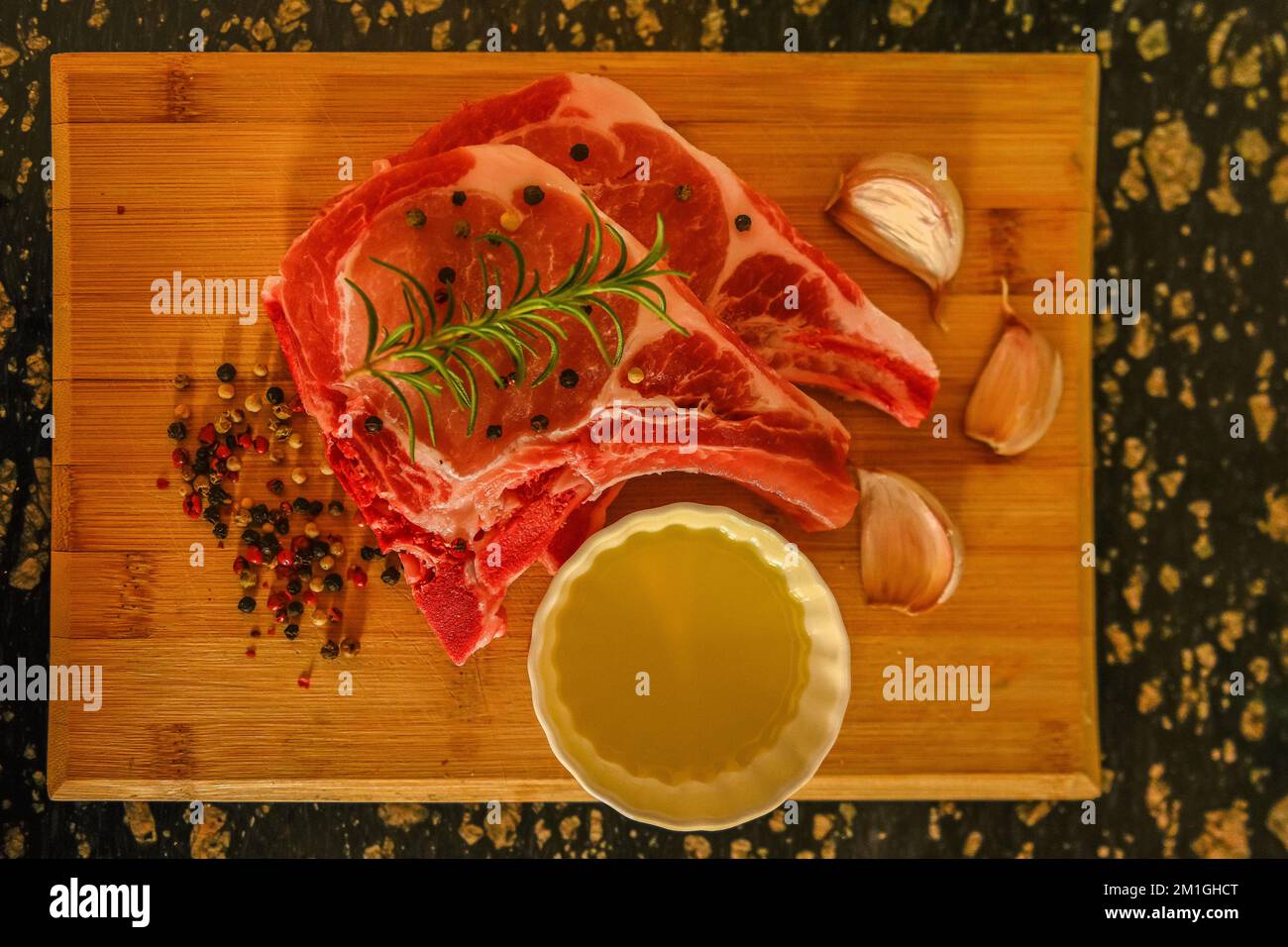 Rohes Schweinekotelett, auf einem Brett, mit Knoblauch, Rosmarin, Öl und Gewürzen Stockfoto