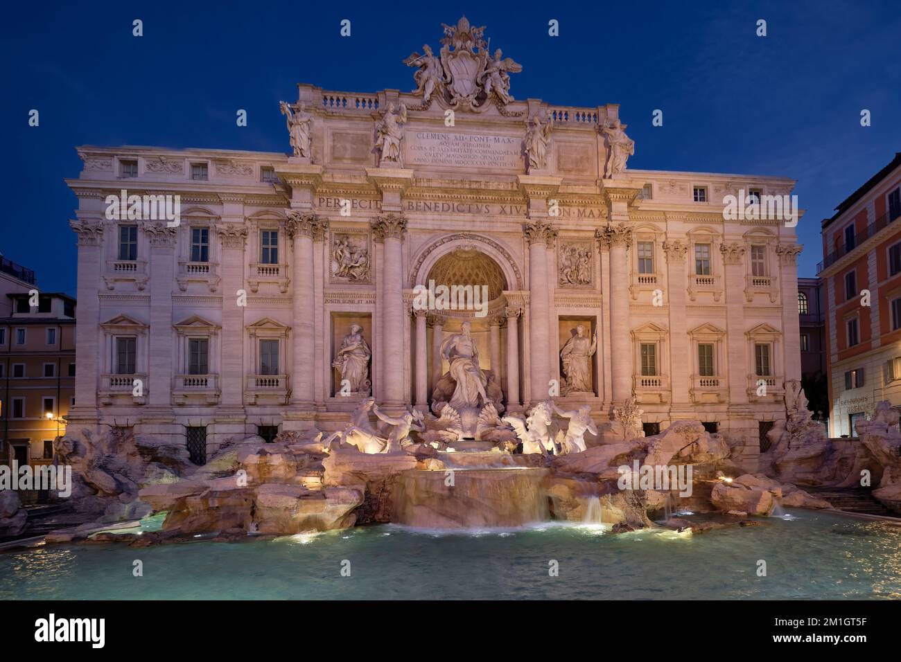 Ein voller Blick auf den Trevi-Brunnen vor dem Palazzo Poli, der kurz vor Sonnenaufgang von Lichtern warm beleuchtet wird. Stockfoto