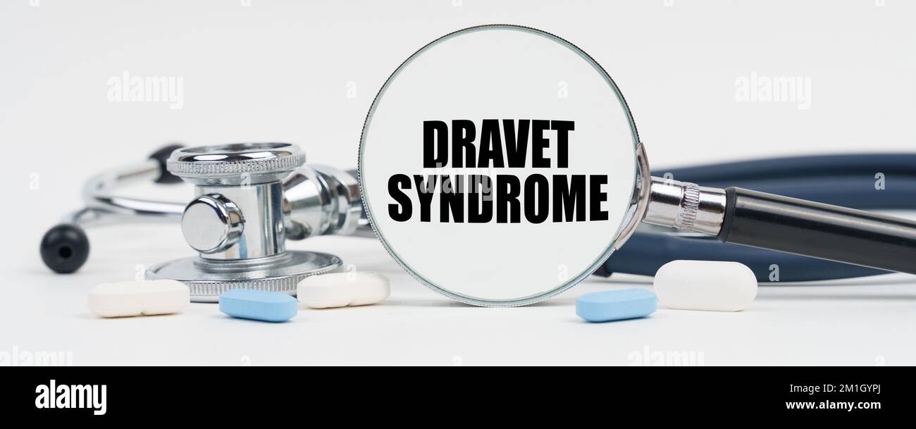 Medizin und Gesundheitskonzept. Auf einer weißen Oberfläche sind Pillen, ein Stethoskop und eine Lupe im Inneren, die geschrieben ist - Dravet-Syndrom Stockfoto