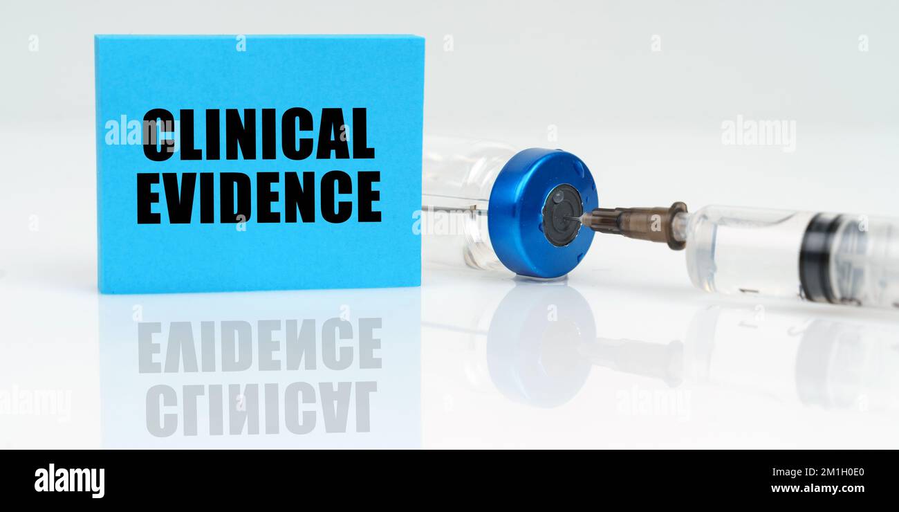 Medizinisches Konzept. Auf einer weißen reflektierenden Oberfläche befinden sich eine Spritze, eine Injektion und eine blaue Plakette mit der Aufschrift - Klinische Evidenz Stockfoto