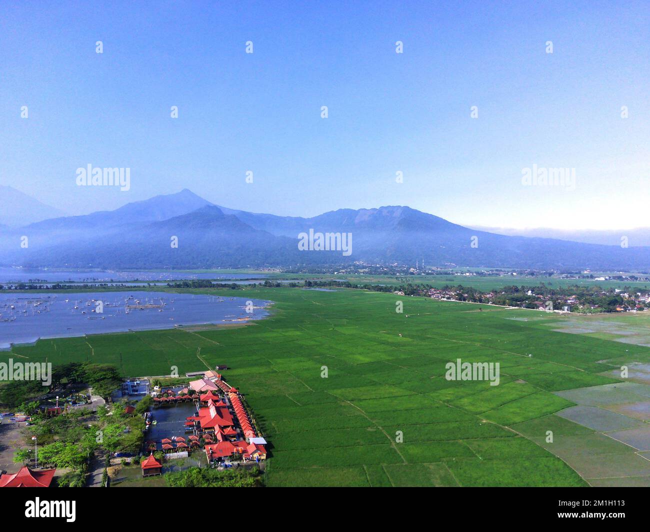 Ein Blick auf die Reisfelder neben roten Gebäuden mit einem See und Bergen in Ambarawa Stockfoto