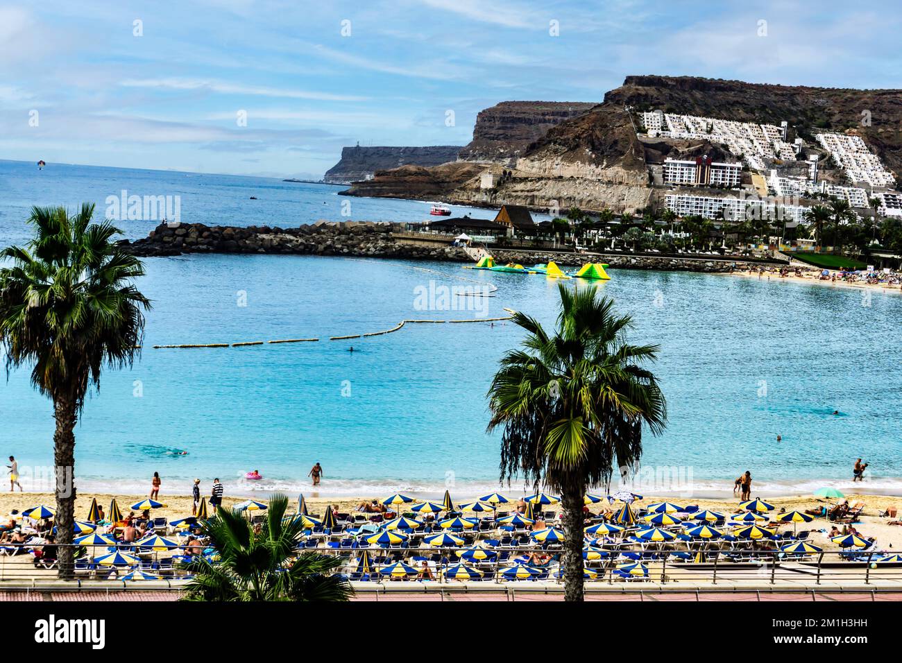 Der lebendige Strand und die atemberaubende Landschaft von Playa de Amadores auf Gran Canaria werden mit einem Farbtupfer zum Leben erweckt. Stockfoto
