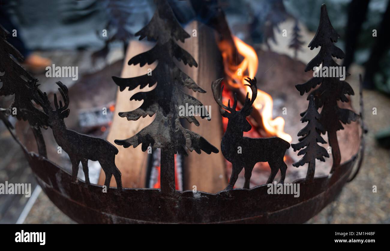 Ein Feuer brennt im ursprünglichen Metallherd mit Figuren von Hirschen und Tannen Stockfoto