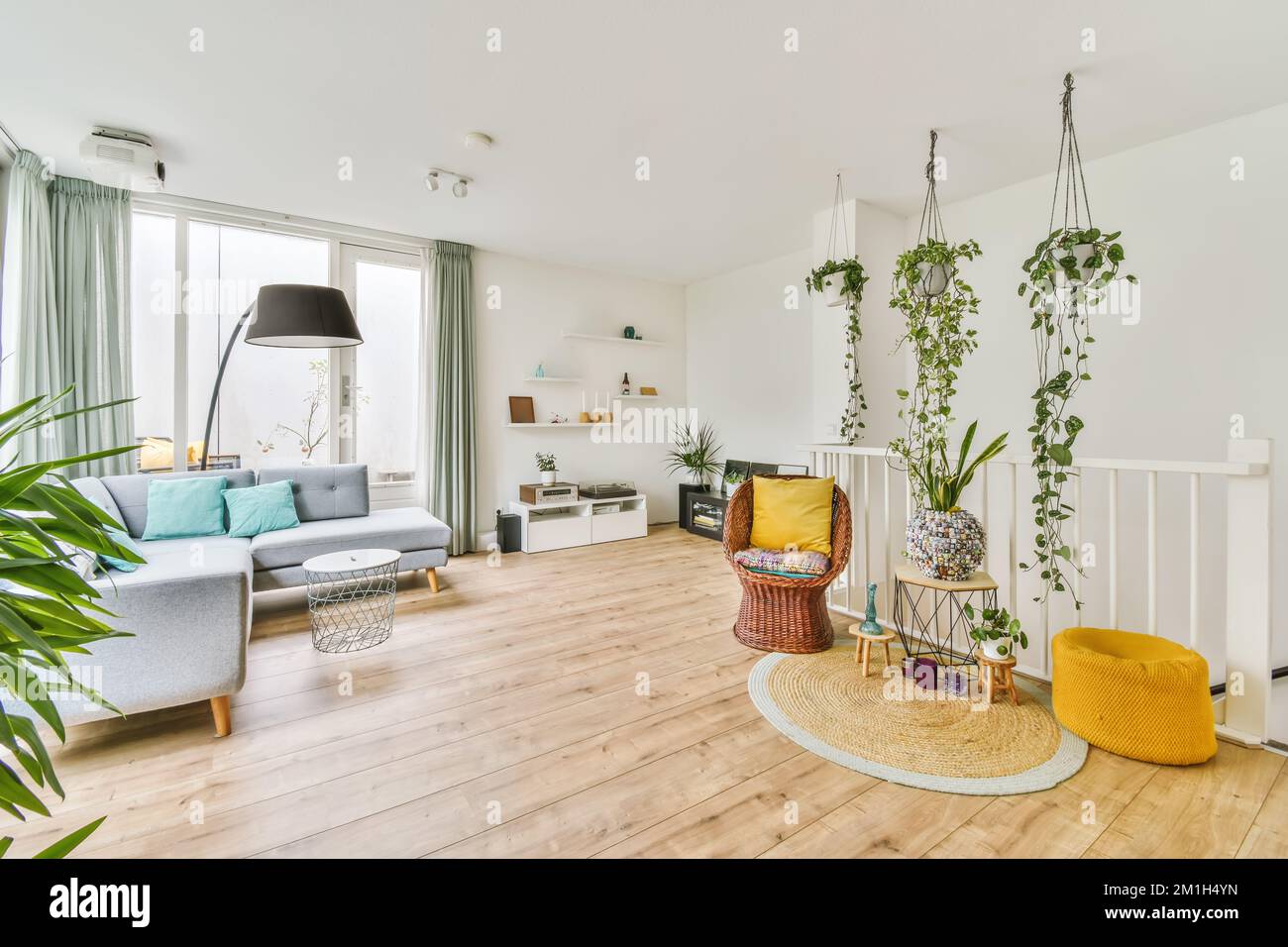 Ein Wohnzimmer mit weißen Wänden und Holzfußboden, Pflanzen in den Ecken auf der rechten Seite der Couch ist gelb Stockfoto