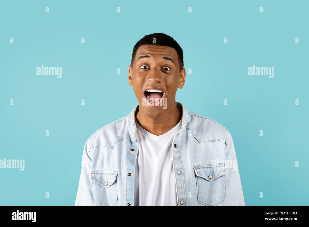 Ein lustiger junger afroamerikanischer Kerl mit offenem Mund, der schreit und in die Kamera schaut, isoliert auf blauem Hintergrund Stockfoto