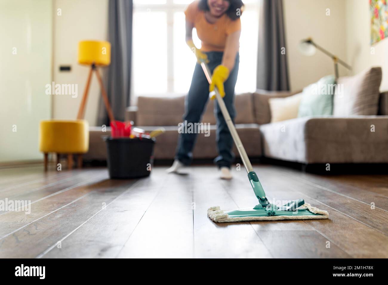 Lächelnde Junge Frau, Waschboden Im Wohnzimmer Mit Mopp Stockfoto