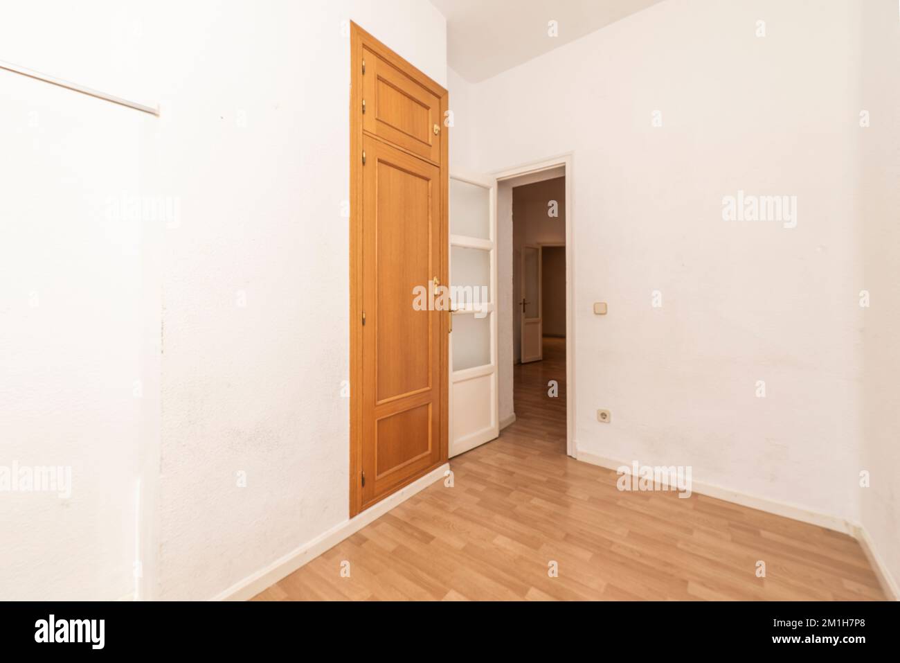 Leeres Zimmer mit Eichenimitationsfußboden, weiß lackierten Massivholztüren mit Glasfenstern und einem schmalen Einbauschrank mit Kofferraum Stockfoto