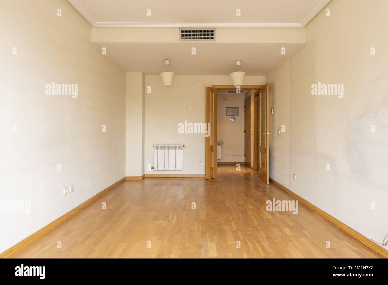 Ein leerer Raum mit Doppelholztüren, einem Aluminiumheizkörper, Klimaanlage durch versteckte Kanäle in der Zwischendecke und Eichenparkettboden. Stockfoto