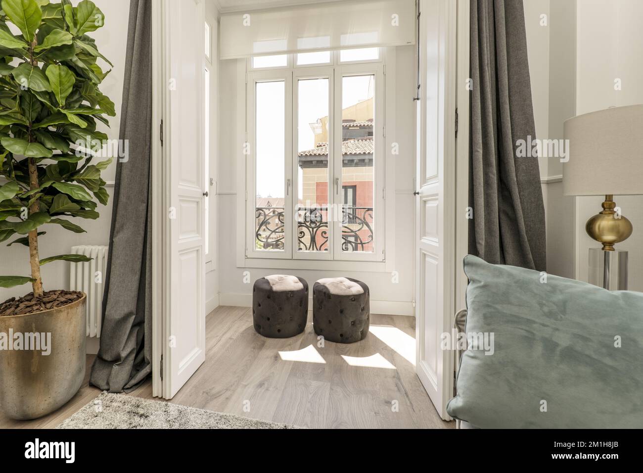 Wunderschönes Haus mit einem weißen Aluminium- und Glaspavillon, Holzläden und einem grauen Samtpouf Stockfoto