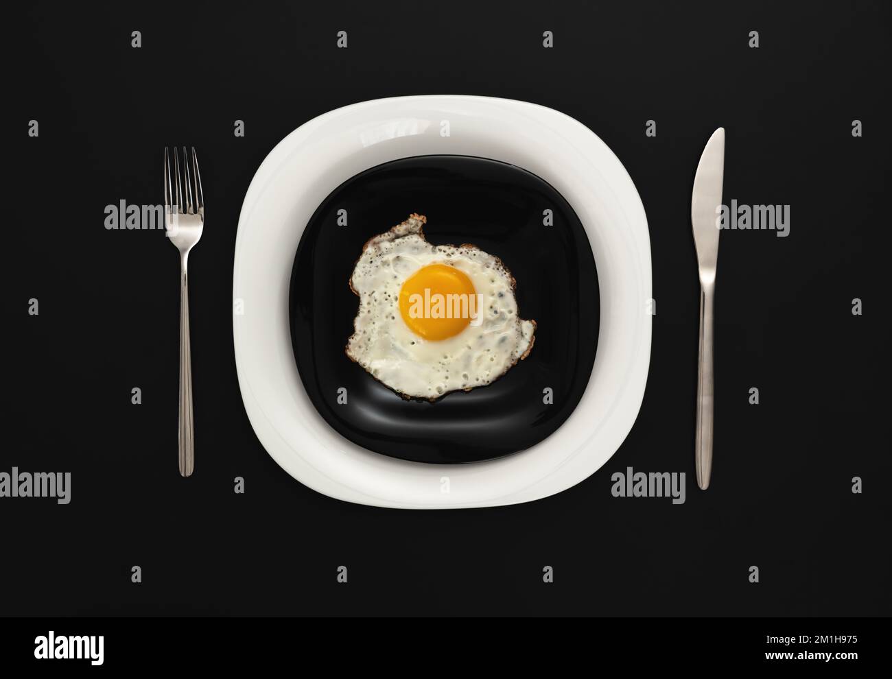Spiegeleier auf einem schwarz-weißen Teller, serviert an einem schwarzen Tisch Stockfoto