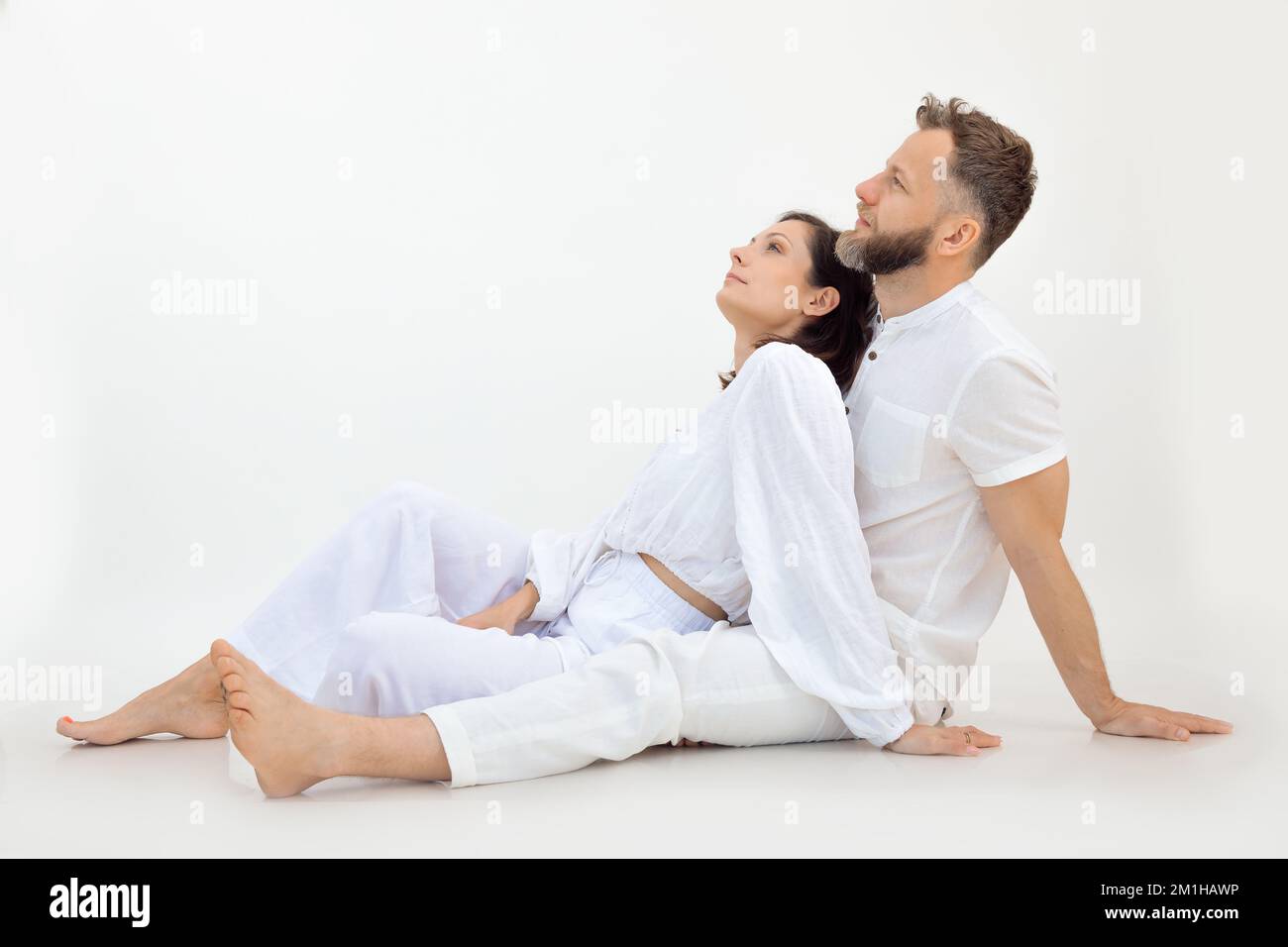 Sportliche Familie, die weiße Kleidung trägt, nach dem Training auf dem Boden sitzt, sich entspannt und auf weißen Hintergrund aufblickt. Liebe. Stockfoto