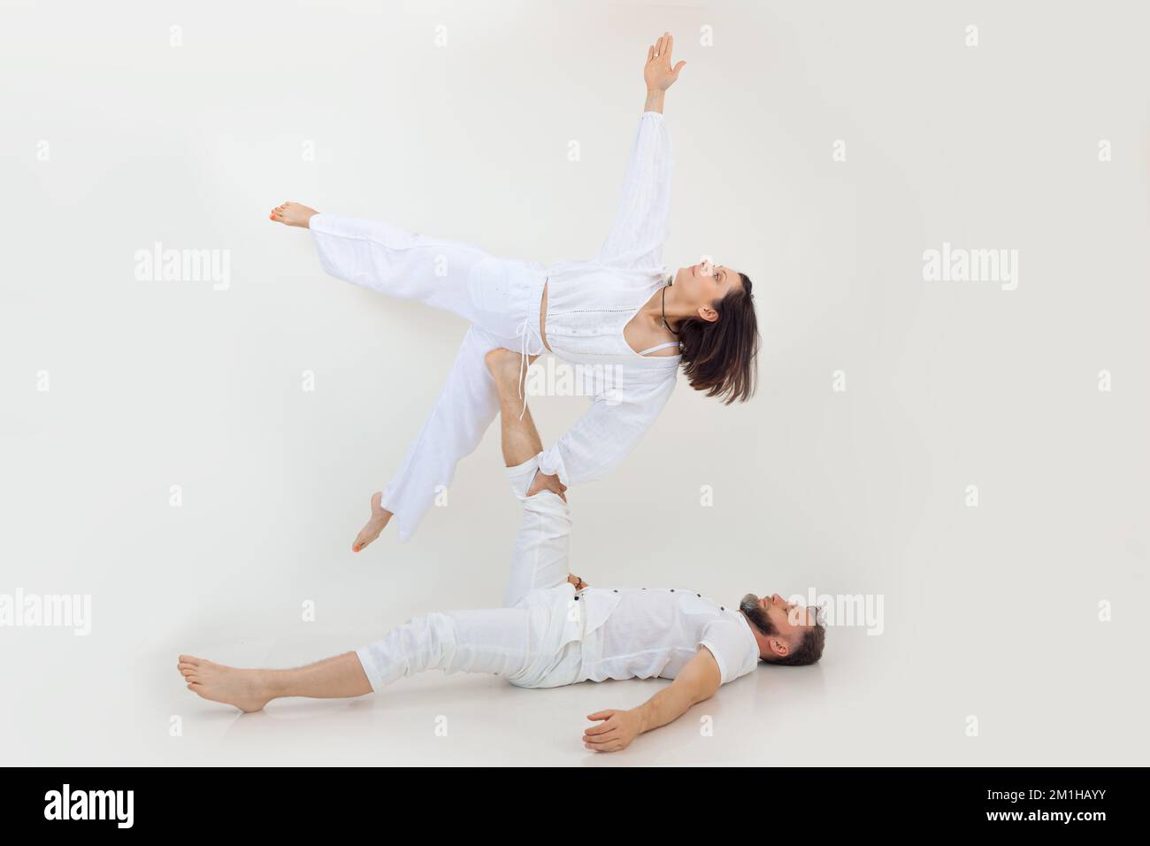 Sportliche Familie auf weißem Hintergrund. Ein Mann mittleren Alters liegt und hält eine junge Frau, die Beine, Arme streckt, acroyoga praktiziert. Stockfoto