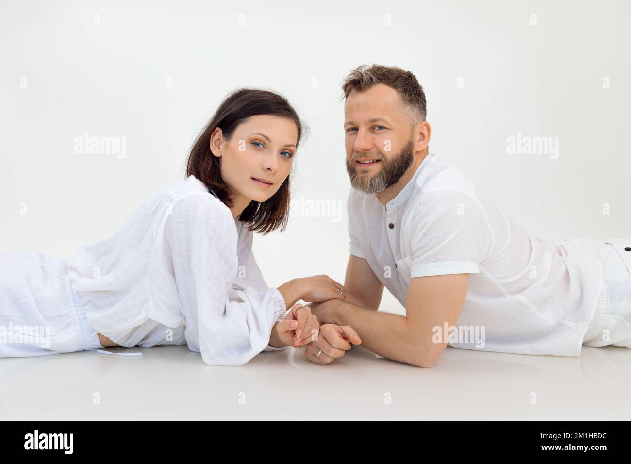Porträt einer sportlichen Familie, die nach dem Training auf weißem Hintergrund liegt. Ein Mann mittleren Alters, der die Hände einer jungen Frau hält. Sport. Stockfoto