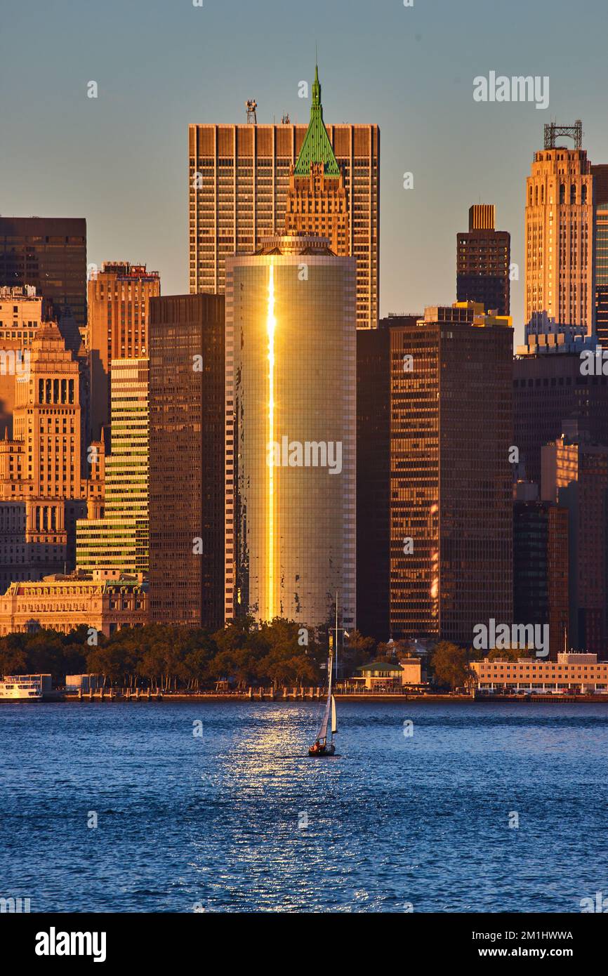 Goldenes Abendlicht über den Wolkenkratzern im Süden Manhattans vom Wasser aus mit einem einzigen Schiff Stockfoto