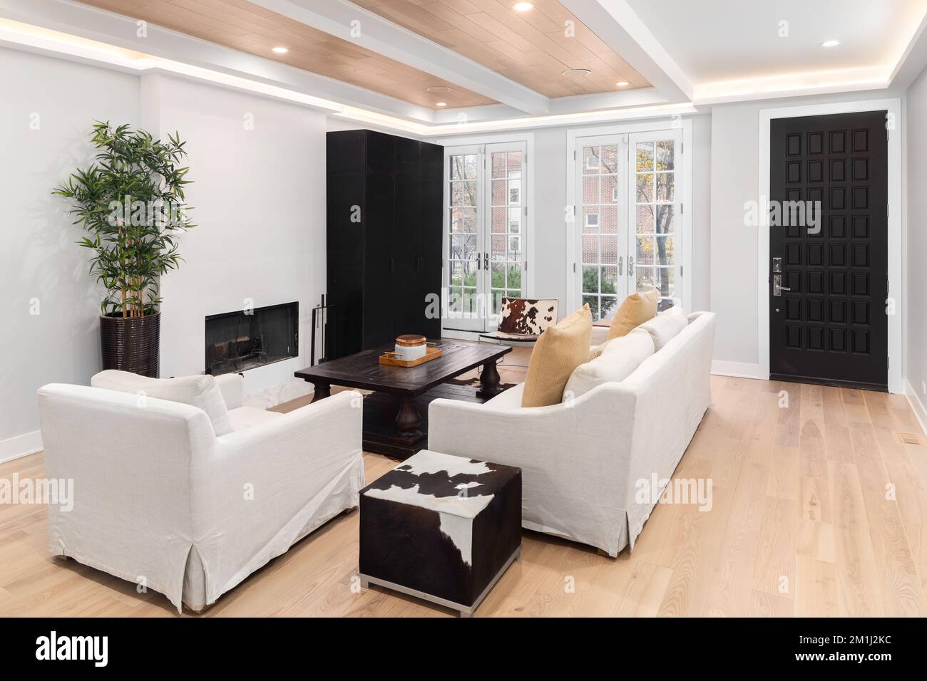 Ein luxuriöses Wohnzimmer mit Hartholzböden, Möbeln vor einem Kamin und Holztäfelung an der Decke. Stockfoto