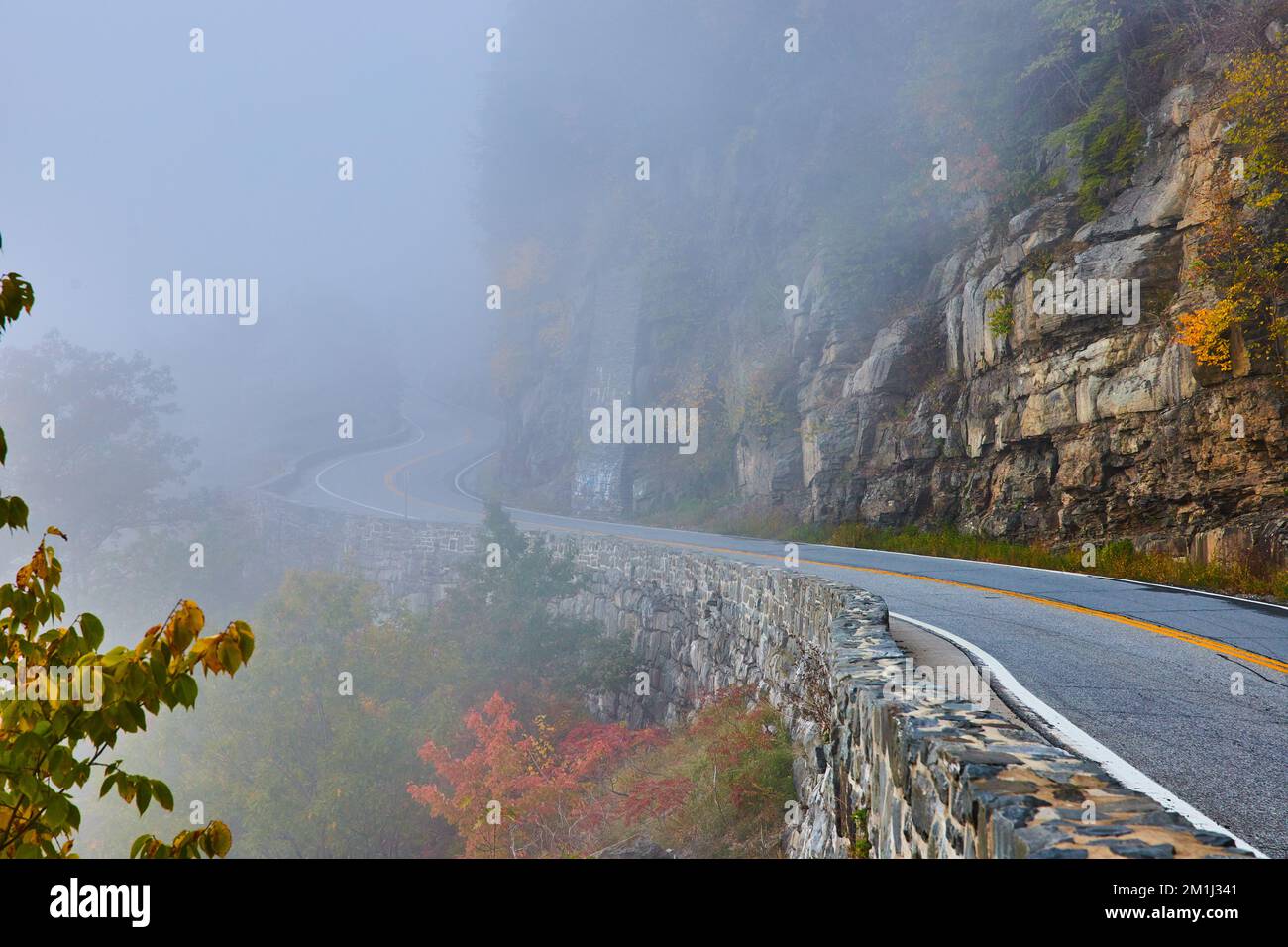 Steinmauer entlang der atemberaubenden Straße gegen die Klippen, die sich in Nebel verschlängeln Stockfoto