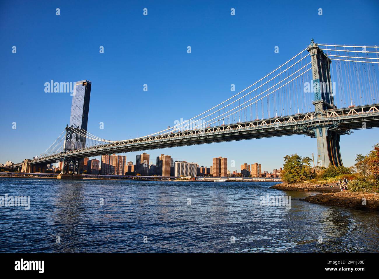 Blick auf die gesamte Manhattan Bridge von Brooklyn in New York City über Wasser mit blauem Himmel Stockfoto