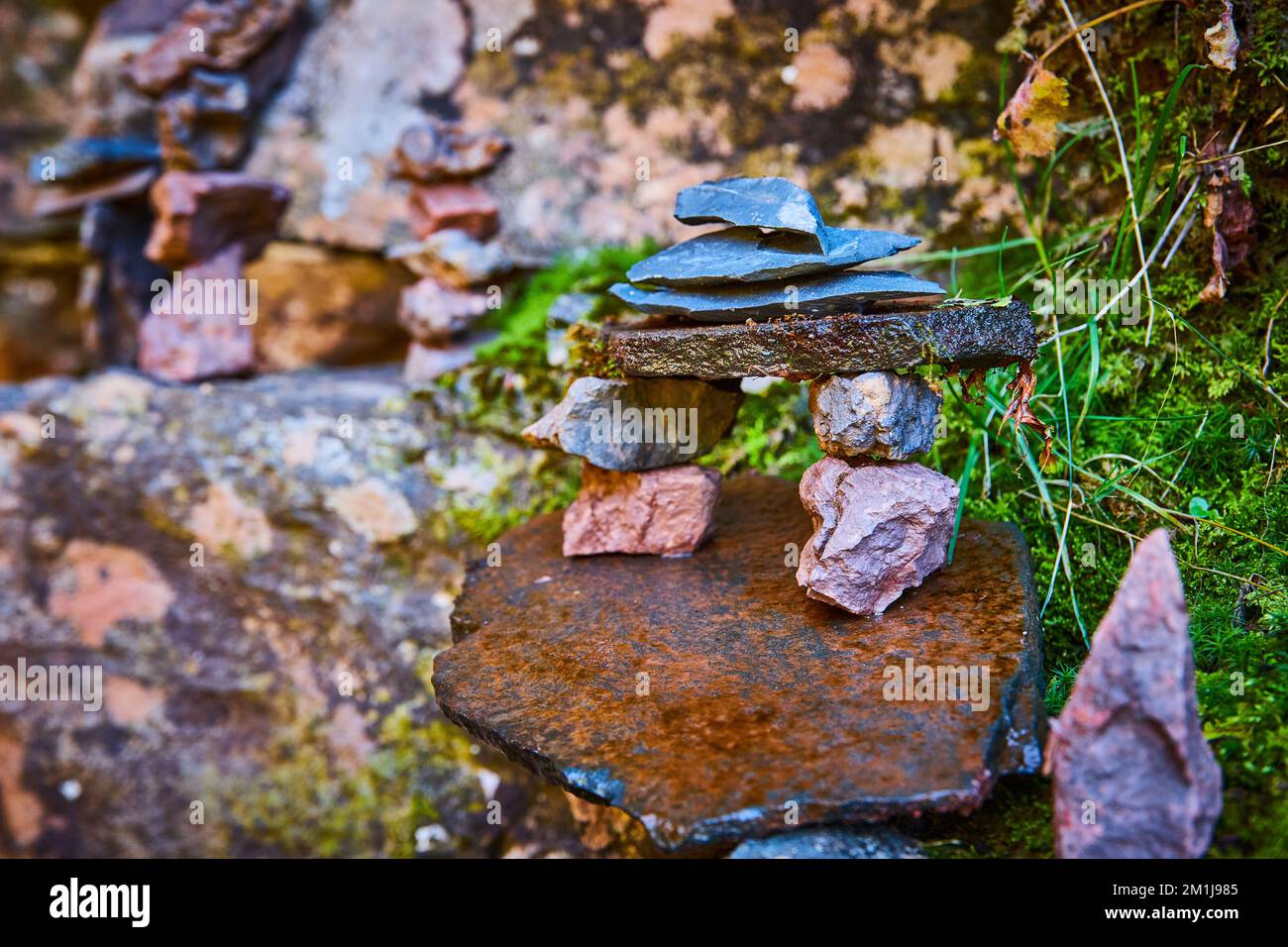 Kleine Steinsteine gestapelte Cairn in wunderschöner Form gegen Flechten bedeckte Steine und Moos Stockfoto