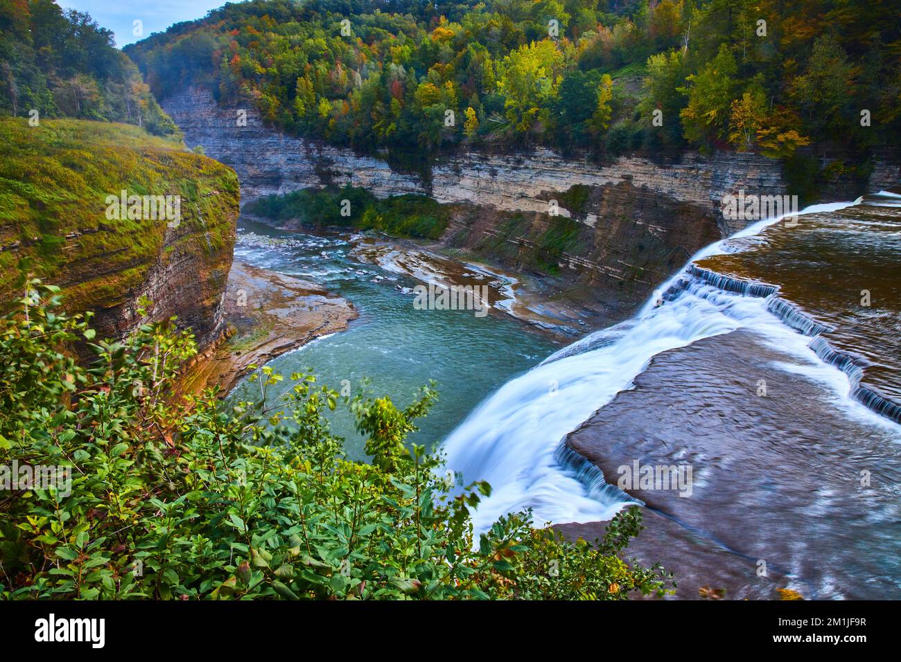 Atemberaubender Wasserfall am Rand, der sich in einen riesigen Canyon mit Klippen und frühem Herbstwald ergießt Stockfoto