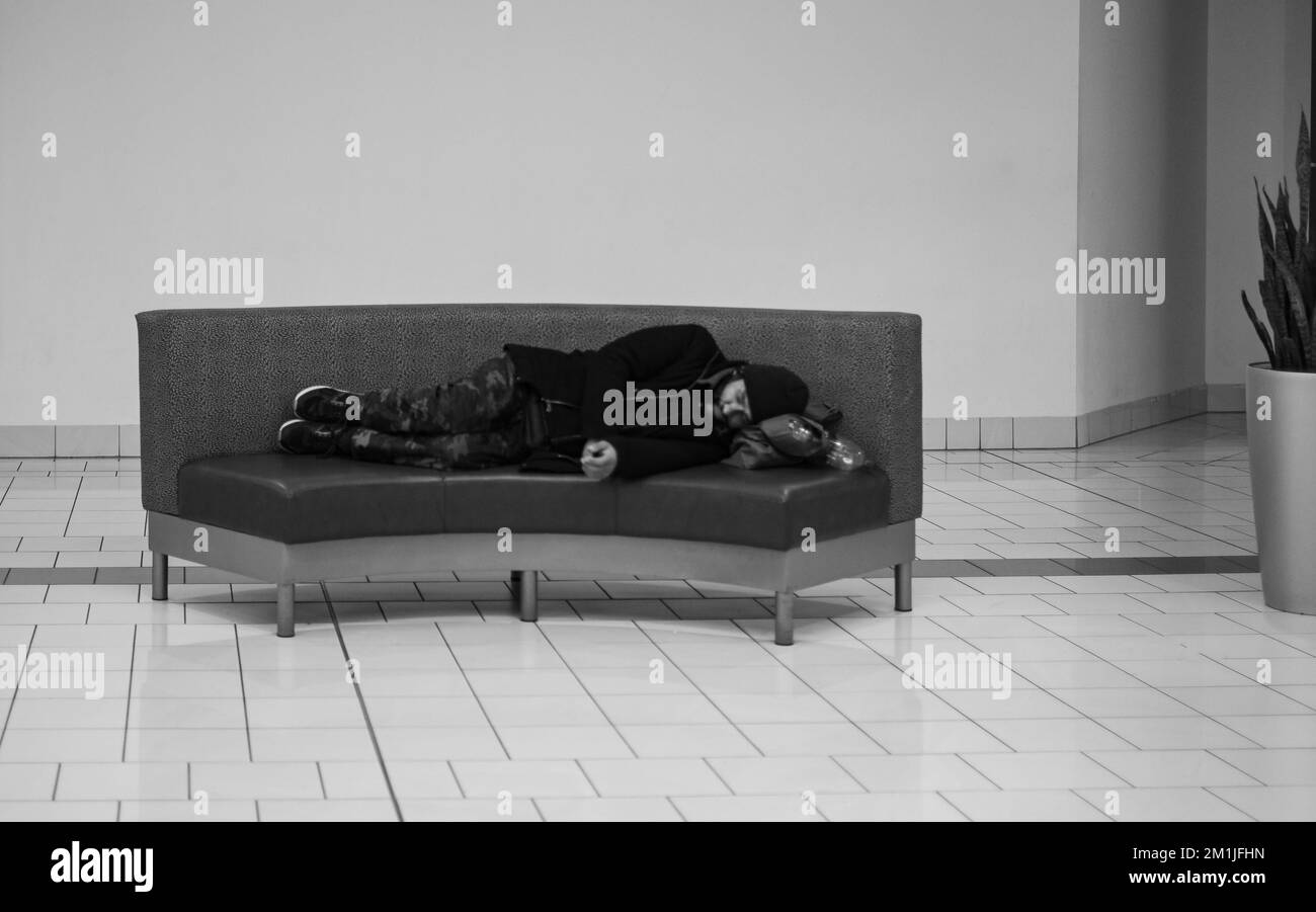 Ein Obdachloser schläft auf einer Bank im Einkaufszentrum. Obdachloser Bettler, der drinnen auf einer Bank liegt, schläft - 8,2022. dezember - Surrey BC Kanada Stockfoto