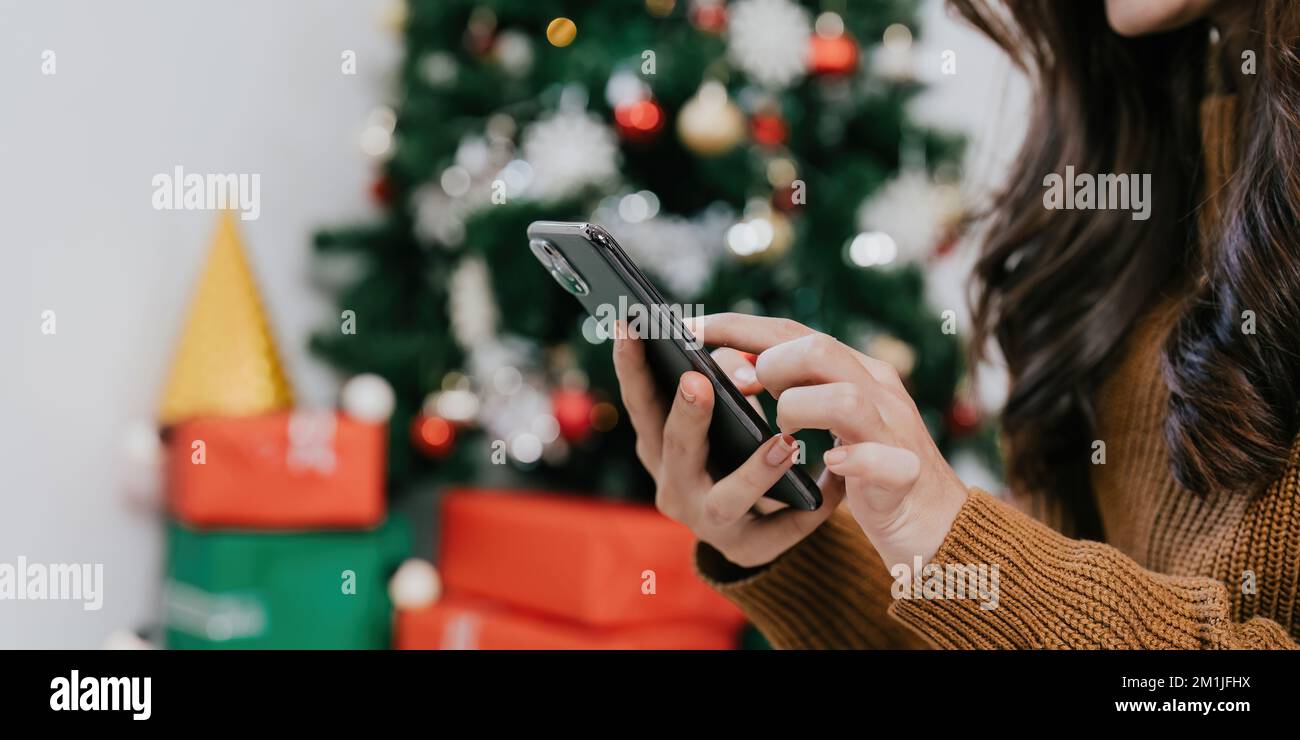 Nahaufnahme der Hand einer Frau, die ihr Mobiltelefon zu Hause verwendet. Bokes weihnachtsbaum-Hintergrund Stockfoto