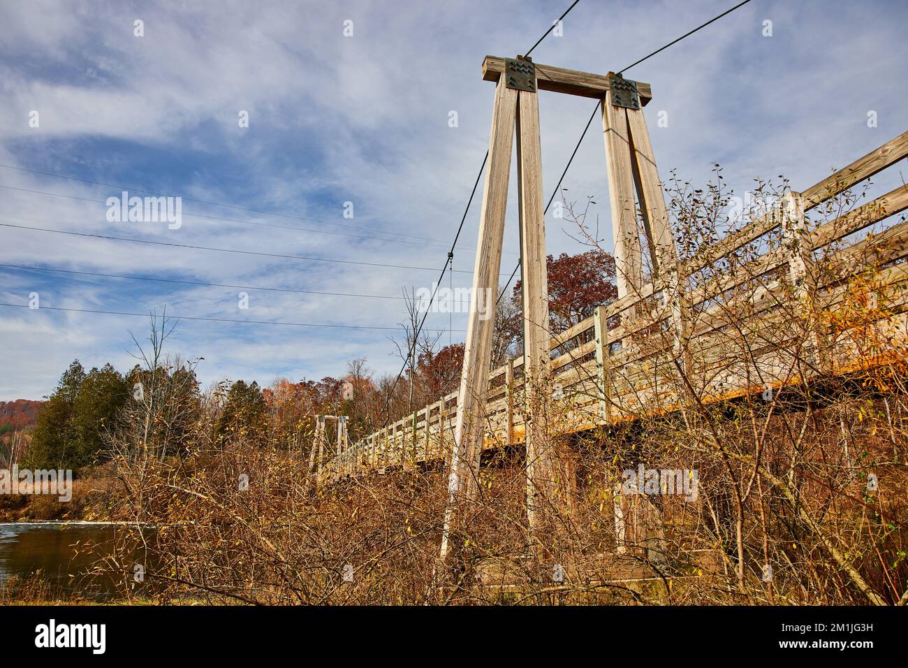 Blick unter die große Hängebrücke über den Fluss in der Nähe von Herbstfeldern und Wäldern Stockfoto