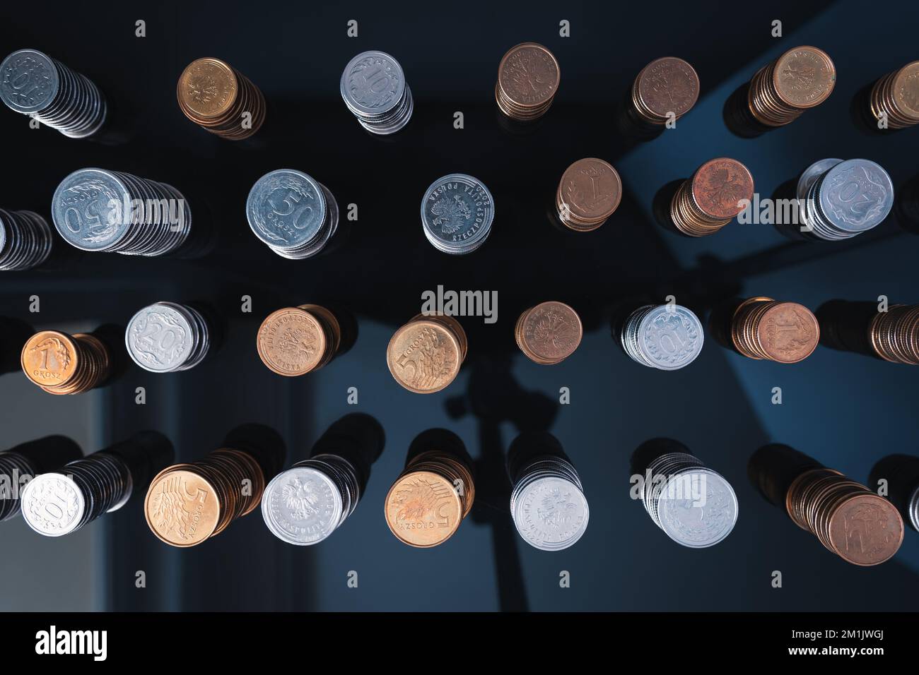 Stapel von Münzen (Polish Zloty, Grosze, PLN) auf einer schwarzen, reflektierenden Oberfläche, von oben gesehen. Inflation verschlingt unsere Ersparnisse. Schwierige Wirtschaftslage Stockfoto