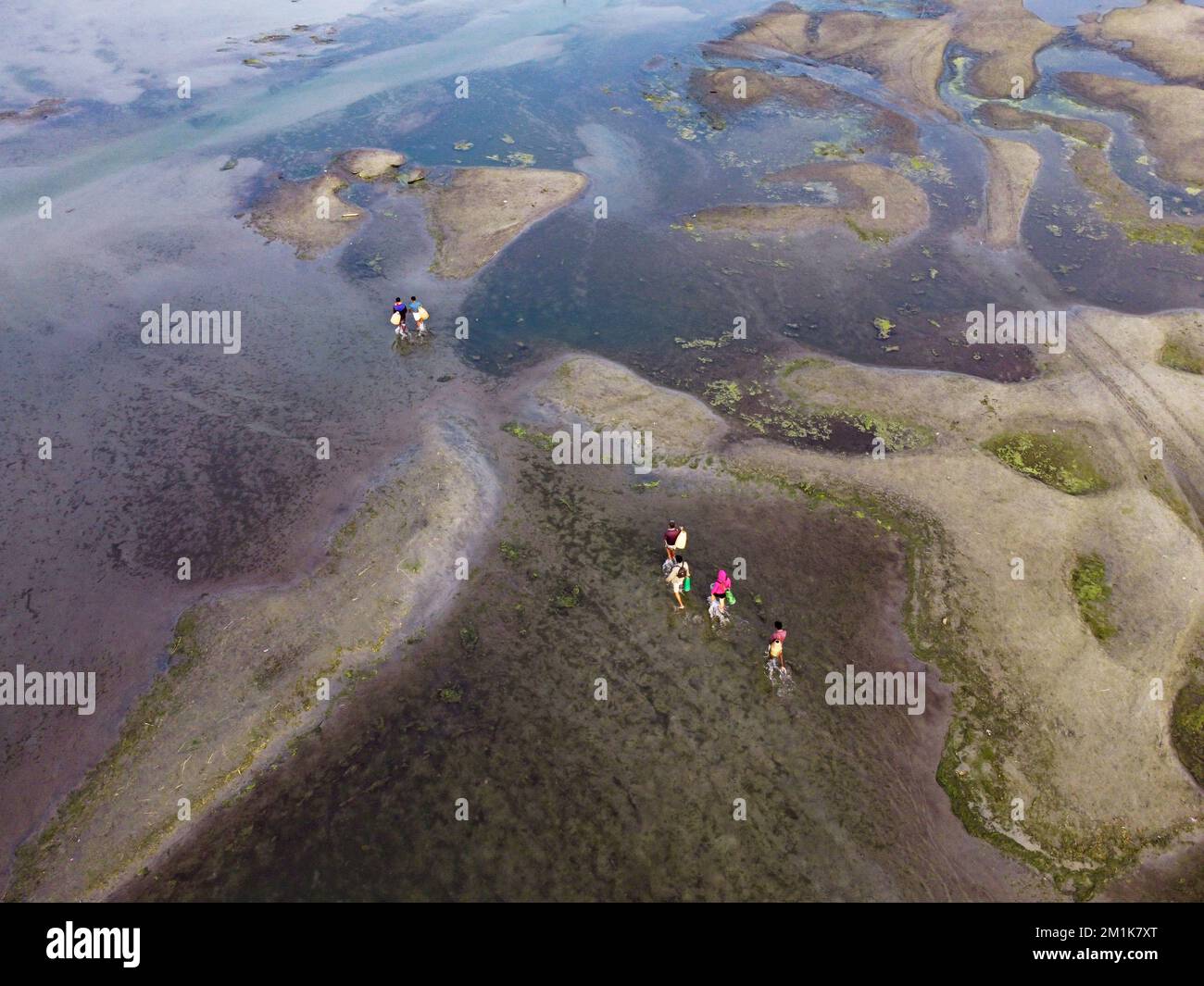 Bogura, Rajshahi, Bangladesch. 13.. Dezember 2022. Passagiere überqueren ein trockenes Flussbett zu Fuß in der Nähe des Jamuna River in Bogura, Bangladesch. Die meisten Wasserstraßen entlang des Jamuna-Beckens im Norden von Bangladesch sind bereits ausgetrocknet und haben riesige Sandbänke geschaffen, die die Boote und die Fahrgastbewegungen stören. Die Sandbänke, in Bengali als „chars“ bezeichnet, haben keine feste Position. Der Fluss legt sie in einem Jahr ab, sehr oft zur späteren Zerstörung, und legt sie in der nächsten Regenzeit wieder ab. Pendler müssen auf der Suche nach befahrbaren Zweigen des Flusses einen weiten Weg zurücklegen. Das sind sie Stockfoto