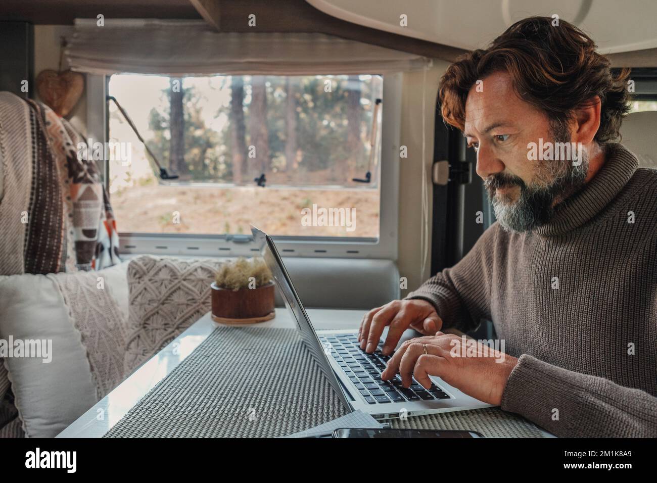 Ein Mann, der in einem Wohnmobil an einem Laptop arbeitet, in einem anderen Büro- und Arbeitsleben. Freiheit für intelligente Arbeiter. Digital Nomad van Life. Stockfoto