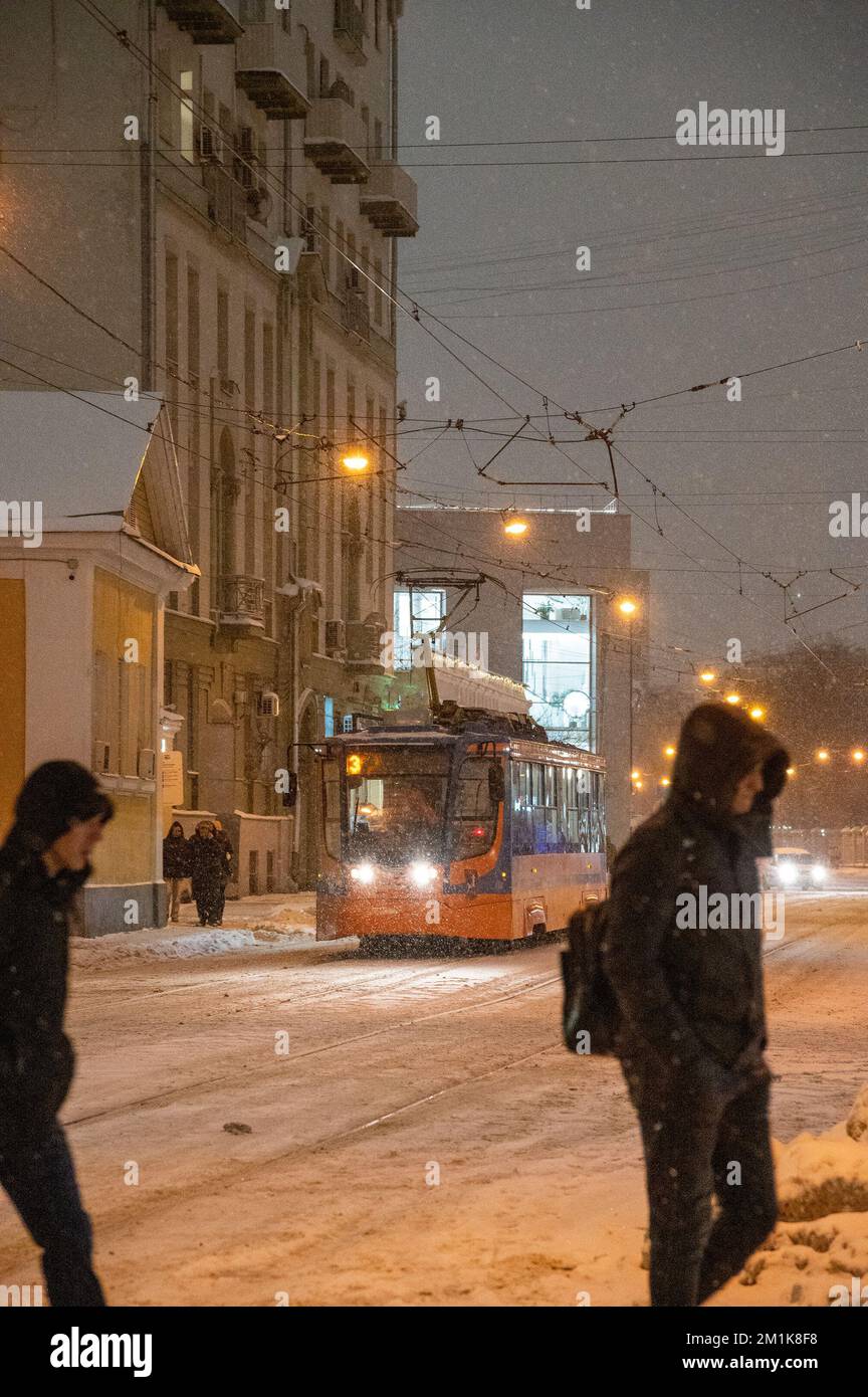 Moskau, Russland - 7. Dezember 2022: Menschen überqueren die Straße in der Nähe der Straßenbahn. Straßenbahnfahrt durch die verschneite Winterstadt Stockfoto