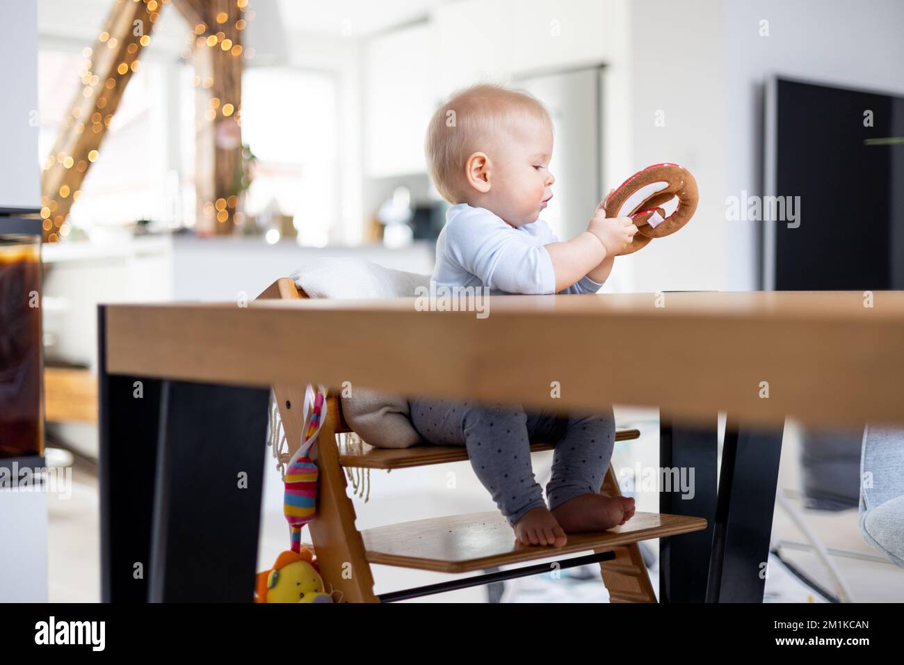 Glückliches Kind sitzt am Esstisch und spielt mit seinem Spielzeug in einem traditionellen skandinavischen Designer-Hochstuhl aus Holz in einem modernen, hellen Wohnhaus. Süßes Baby, das mit Spielzeug spielt. Stockfoto