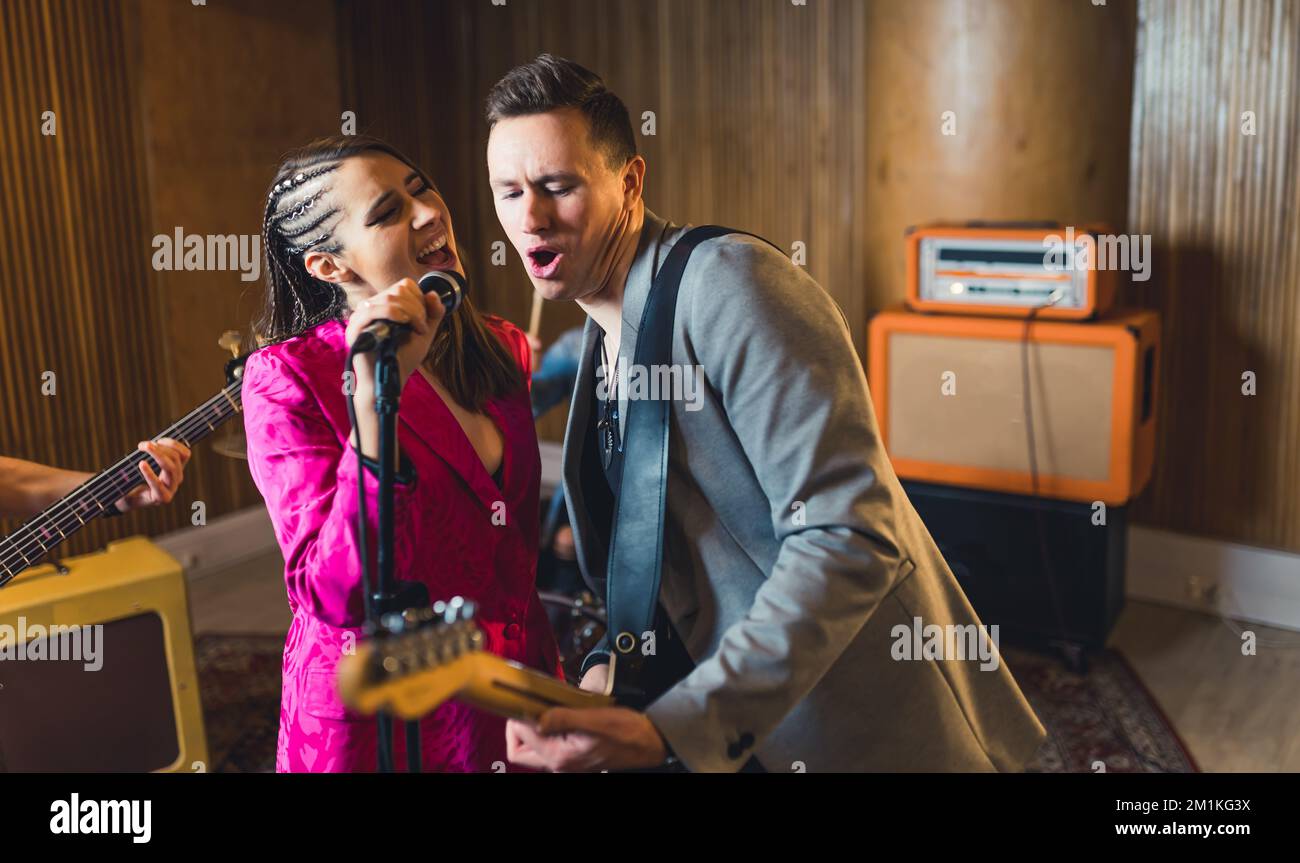 Sänger und Gitarrist. Innenporträt einer Sängerin aus Weißer, die während eines Konzerts mit männlichem Gitarrist ins Mikrofon singt. Hochwertiges Foto Stockfoto