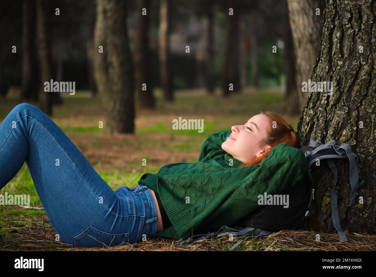 Rothaarige junge Frau, die im Wald unter einem Baum lag. Stockfoto