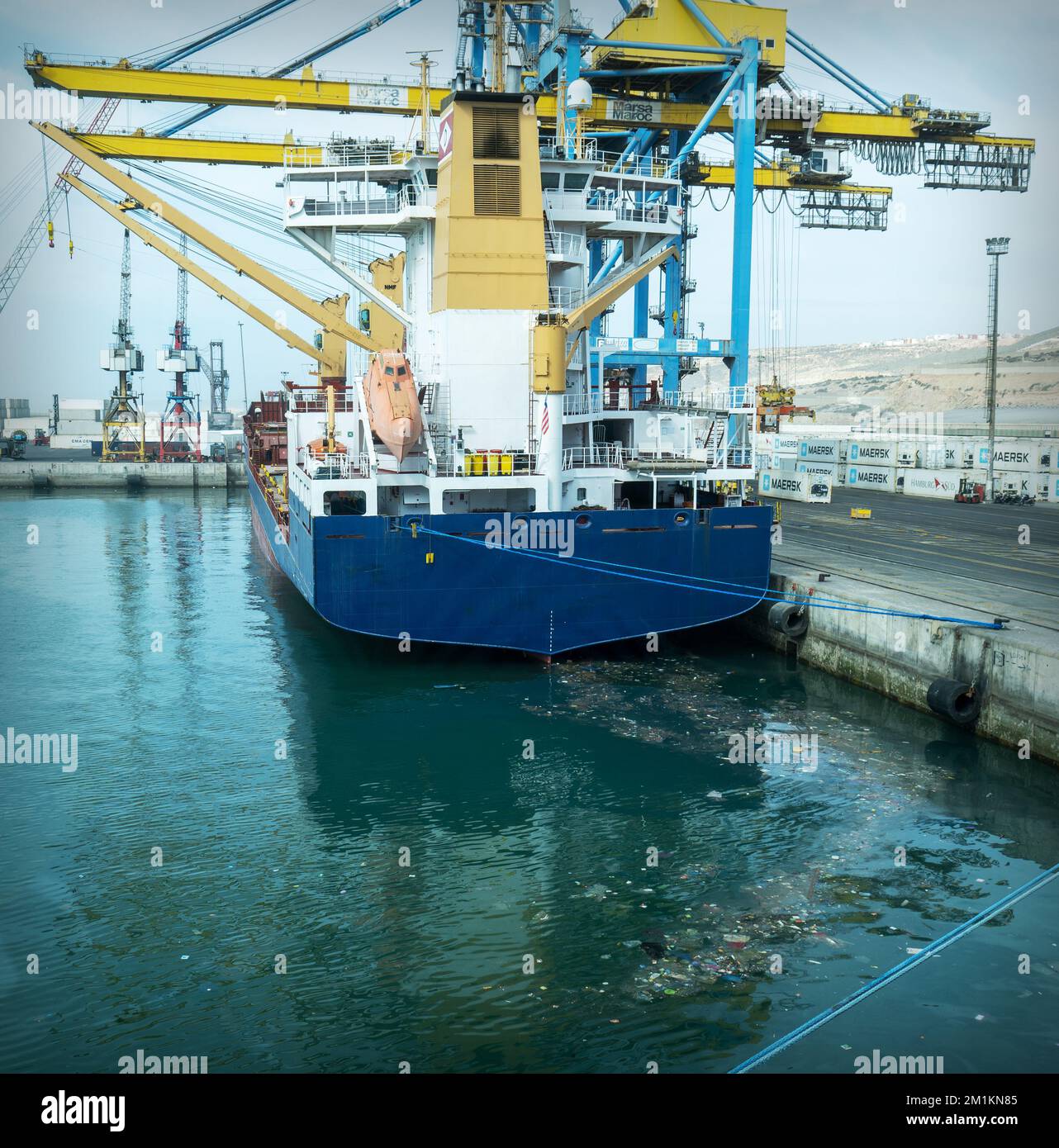 Containerschiff vor Anker im Hafen, in verschmutztem Meerwasser. Stockfoto