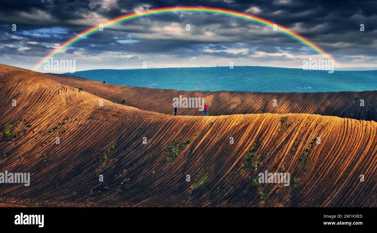 Regenbogen und dramatischer grauer Himmel mit Wolkenlandschaft. Malerisches hügeliges Feld Stockfoto