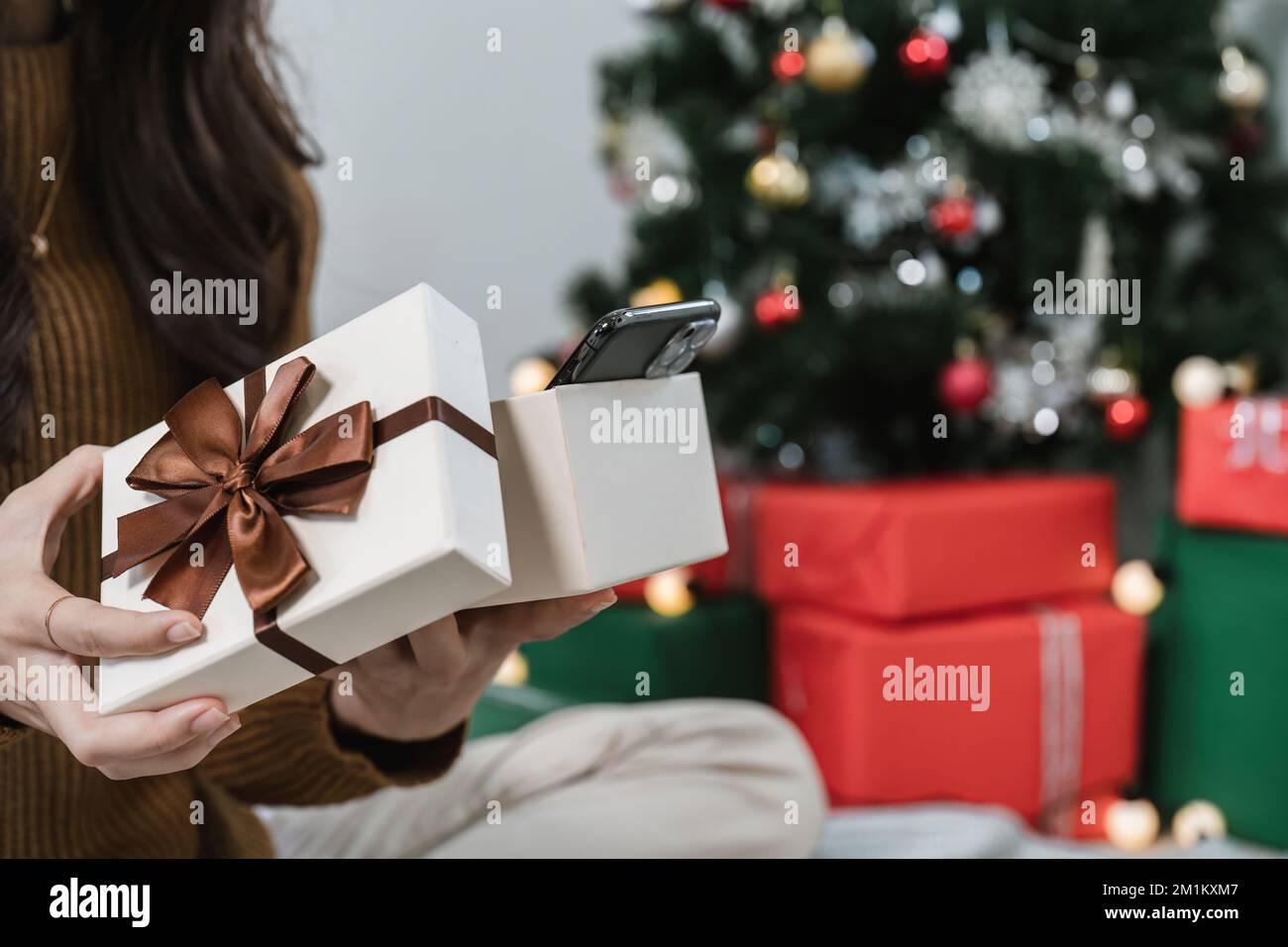 Nahaufnahme Frau öffnet ein Geschenk neben dem Weihnachtsbaum. Frohe Feiertage und Neujahr Stockfoto
