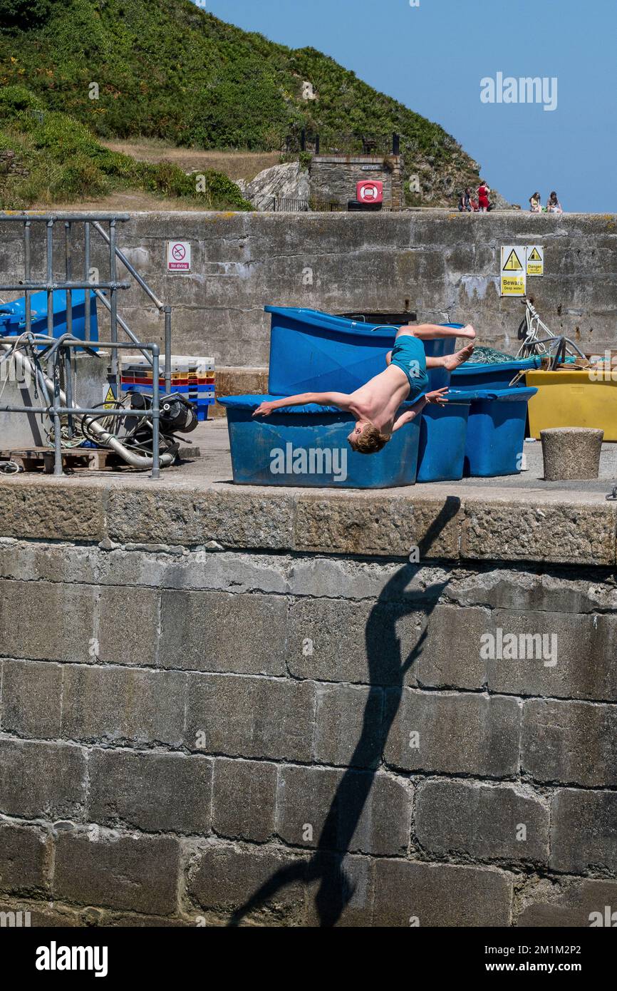 Ein junger männlicher Teenager, der einen akrobatischen Sprung ins Meer am Newquay Harbour in Cornwall in England im Vereinigten Königreich macht. Stockfoto
