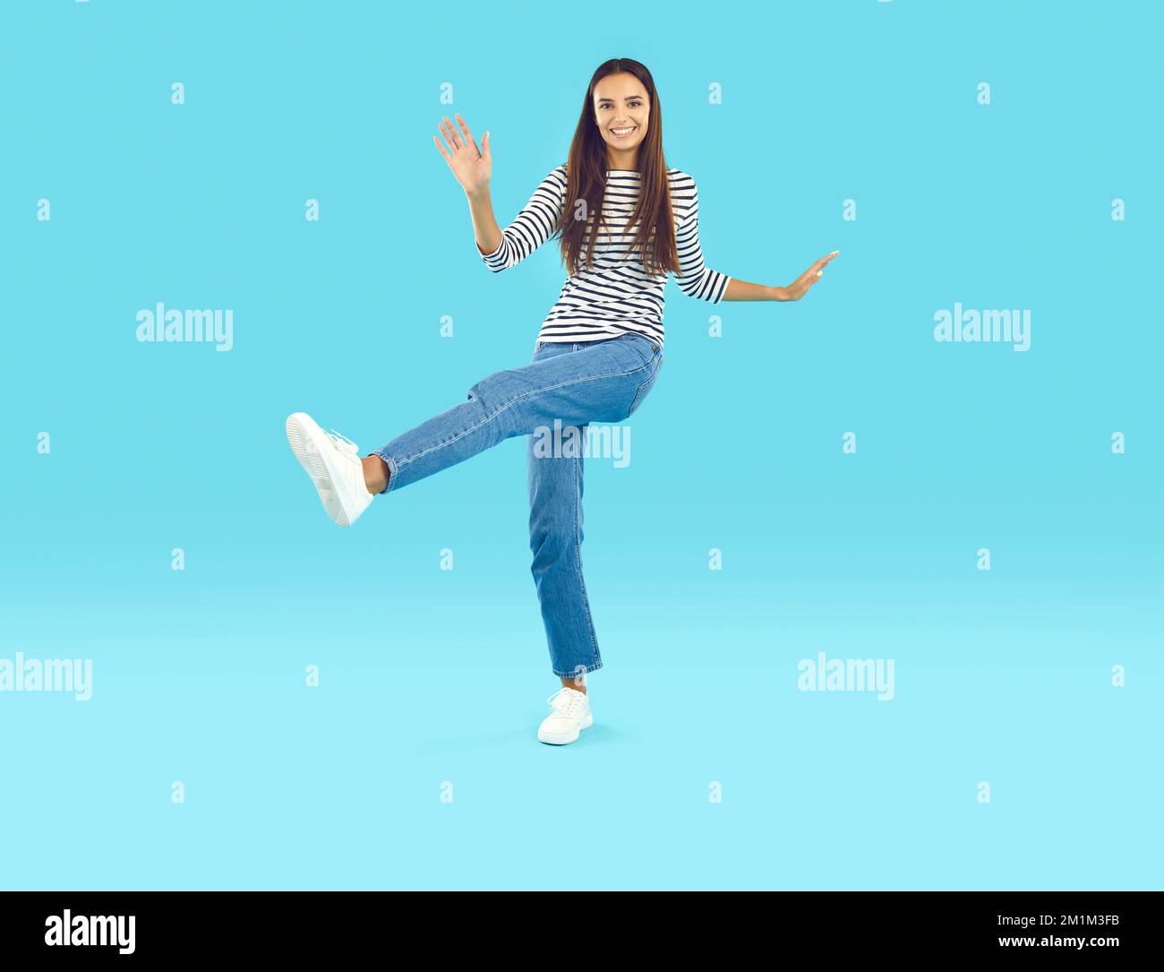 Glückliche, wunderschöne junge Frau in lässigem Outfit, die auf blauem Studiohintergrund tanzt Stockfoto