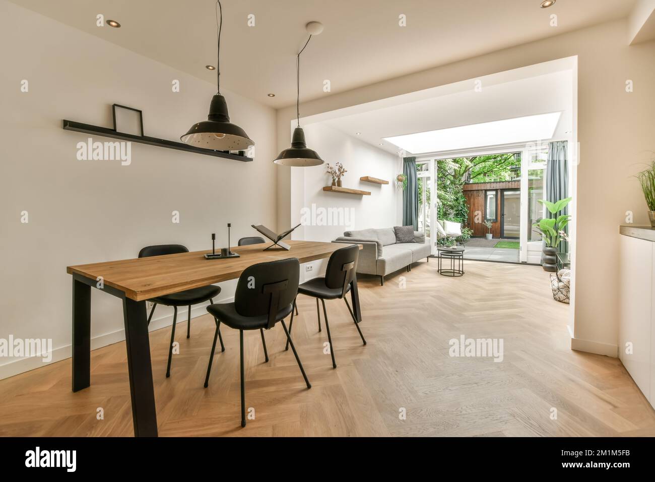 Ein Speisesaal mit Holzfußboden und weißen Wänden, es gibt einen großen Holztisch umgeben von schwarzen Stühlen Stockfoto