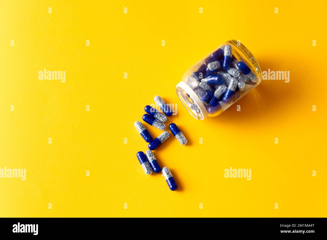 Blaue Vitaminkapseln aus dem Glas auf gelbem Hintergrund Stockfoto