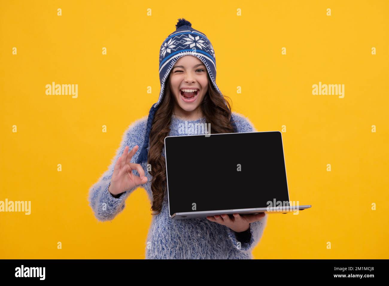 Herbstschule. Teenager-Schülerin in Herbstbekleidung hält Laptop auf gelbem, isoliertem Studiohintergrund. Aufgeregtes Gesicht, fröhliche Emotionen eines Teenagers Stockfoto