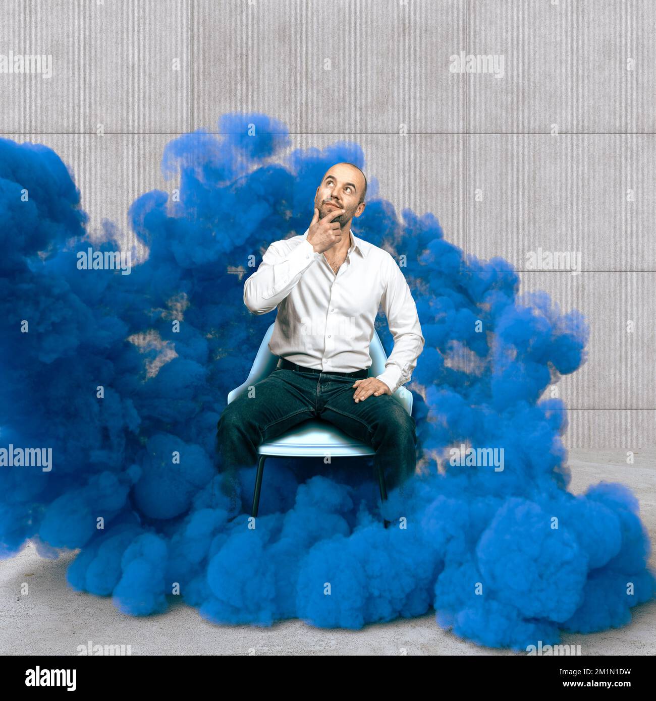 Ein nachdenklicher Mann sitzt eingewickelt in blauem Rauch, Kreativitätskonzept Stockfoto