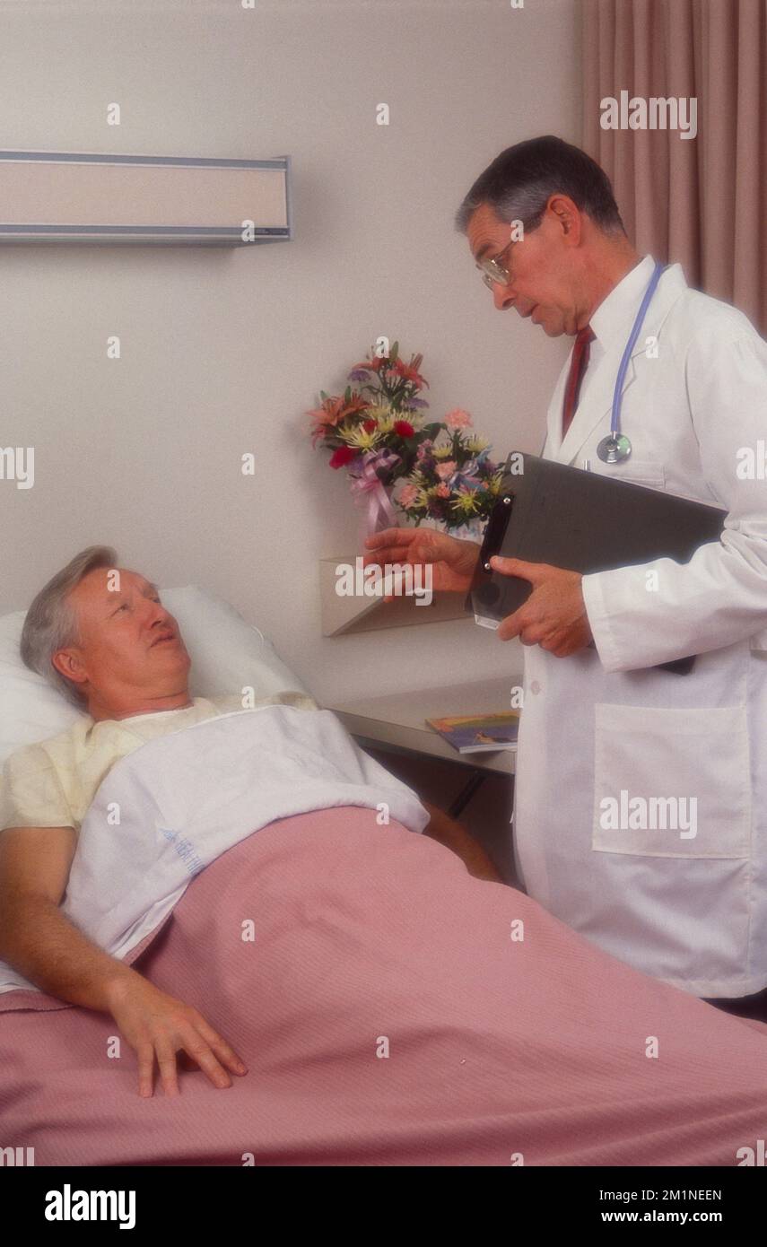 Arzt steht neben dem Krankenhausbett mit älterem Mann, der medizinische Fragen diskutiert Stockfoto