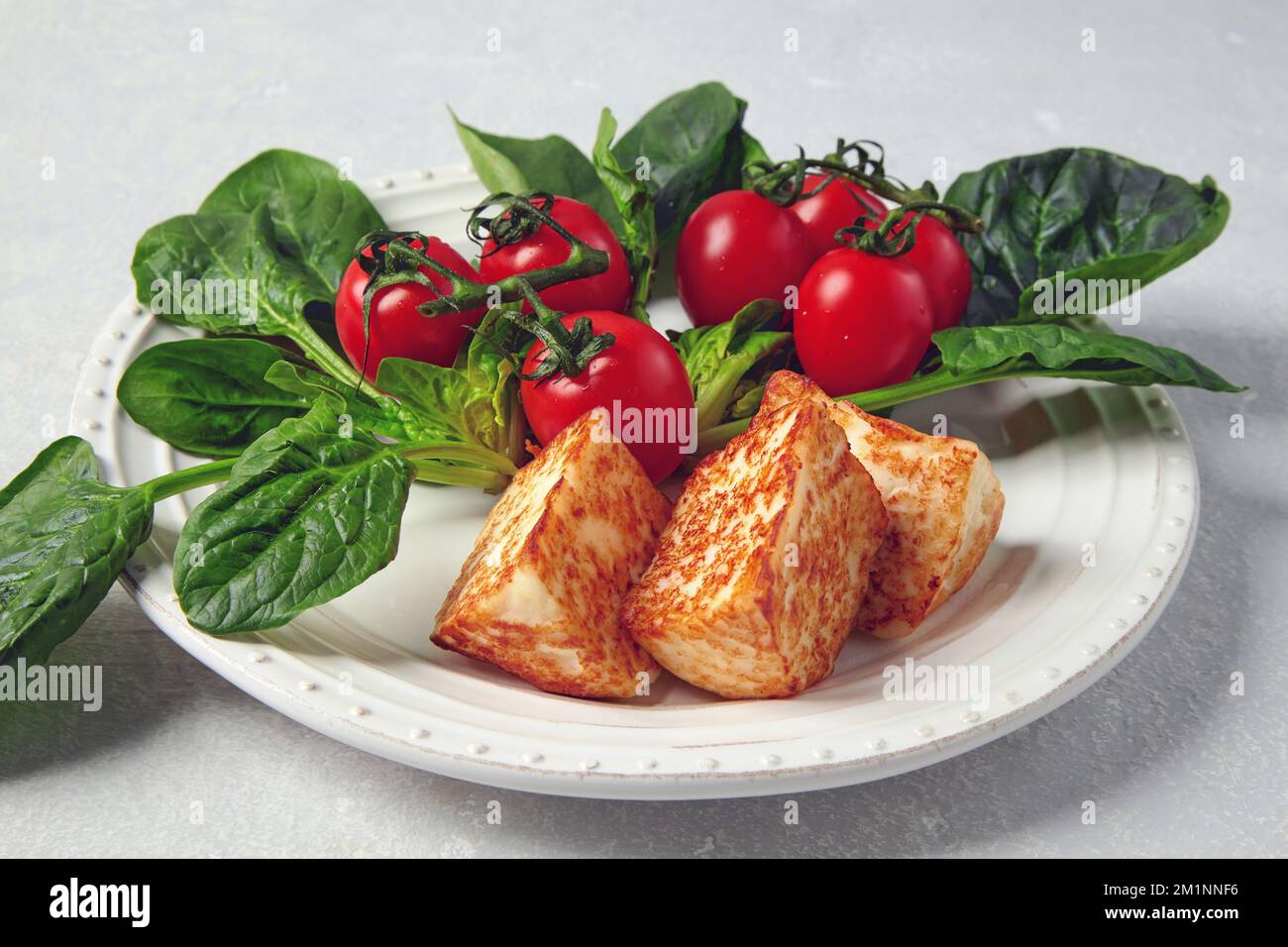 Gebratener Quark Mozzarella halloumi mit Kirschtomaten und grünem Spinat auf einem grauen Betontisch Stockfoto