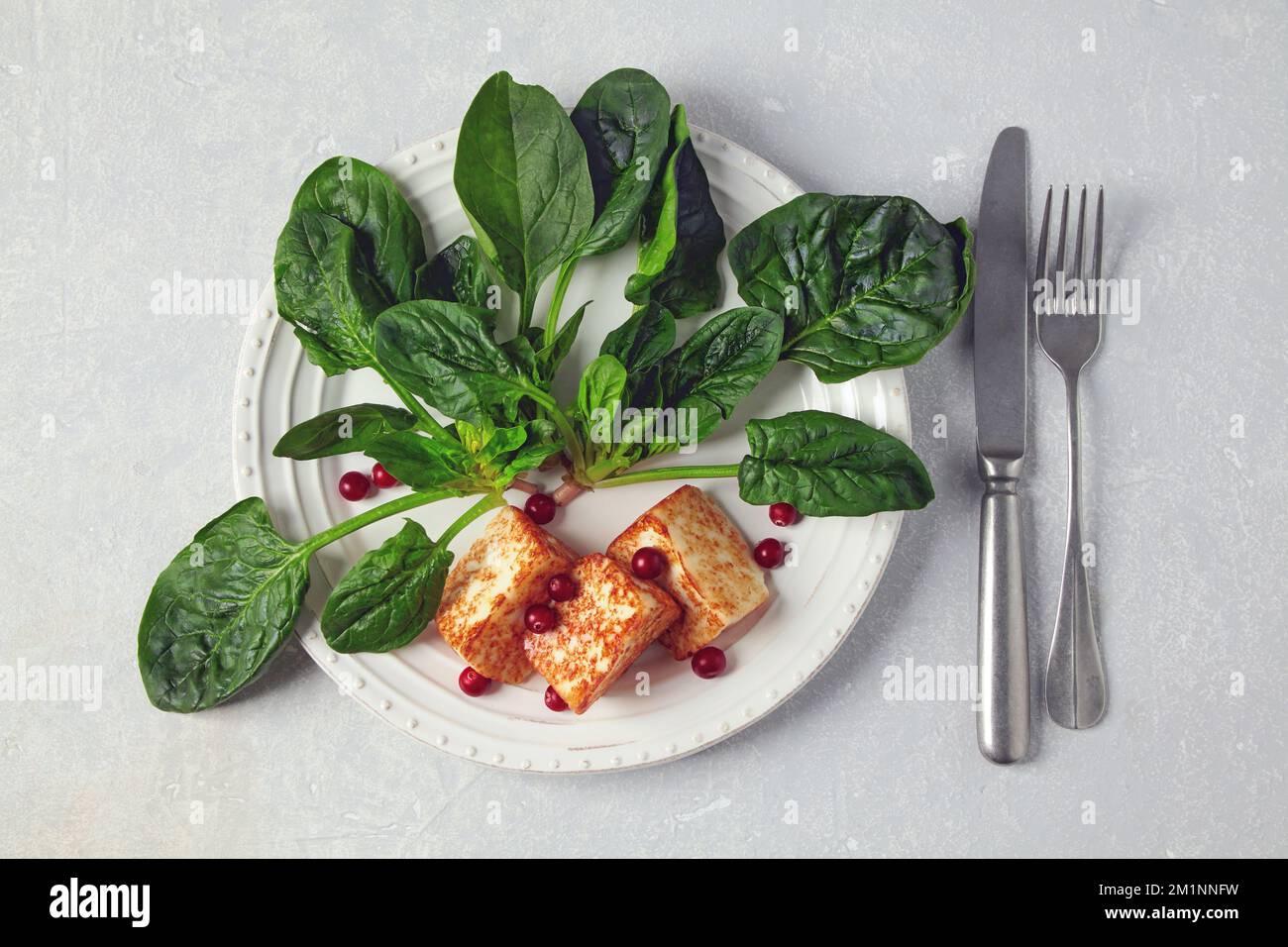 Gebratener Quark Mozzarella halloumi mit grünem Spinat und Preiselbeeren auf einem grauen Betontisch Stockfoto